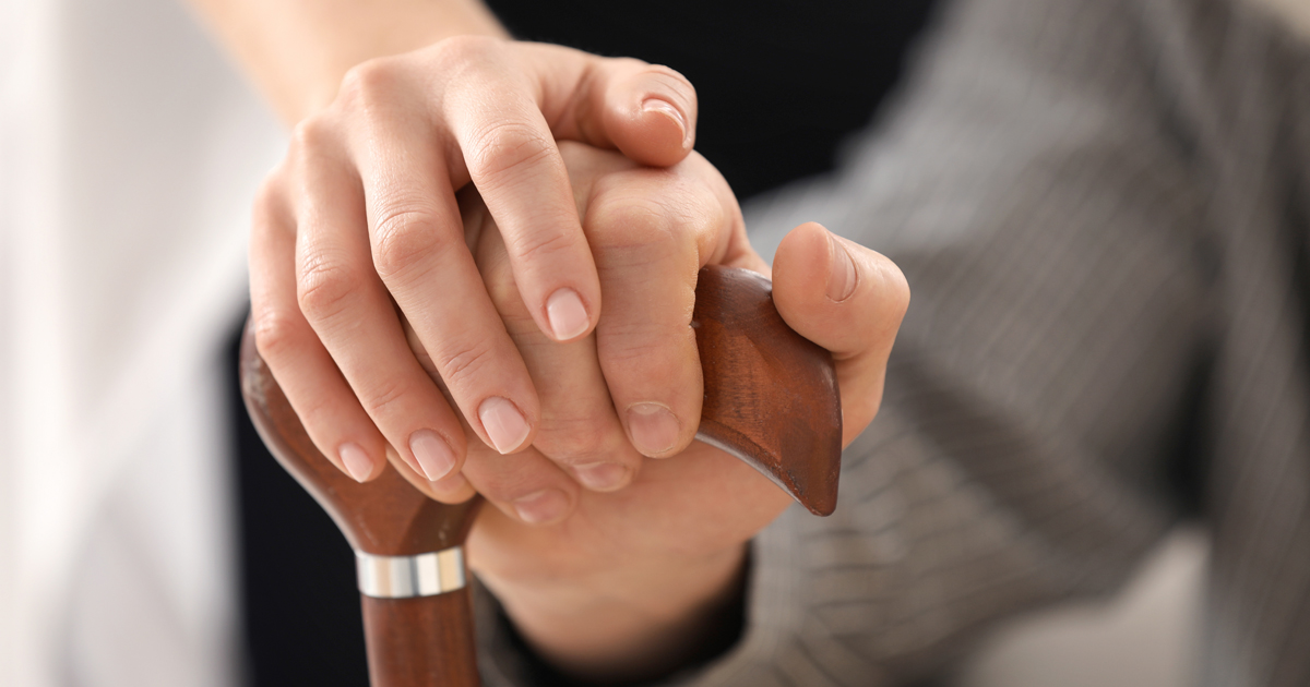 caregiver hand holding resident hand on cane