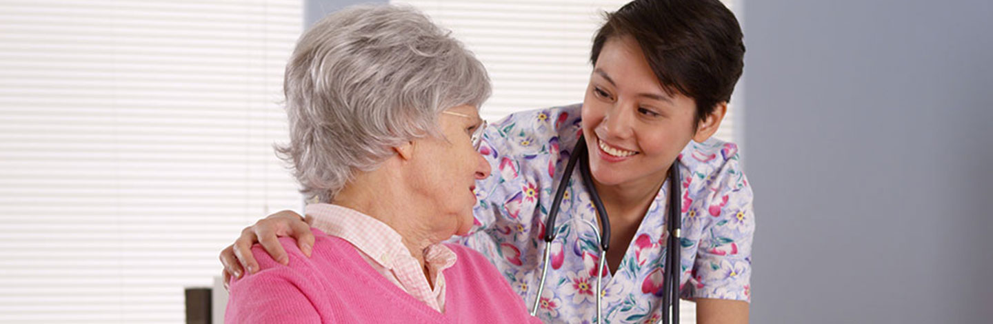 A nurse leans over to talk to an older woman in a wheelchair