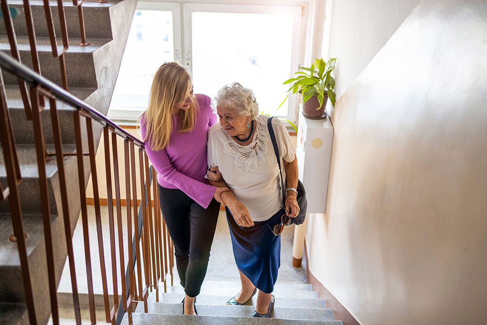 Caregiver helping senior woman up stairs. Read more for tips to avoid caregiver burnout.