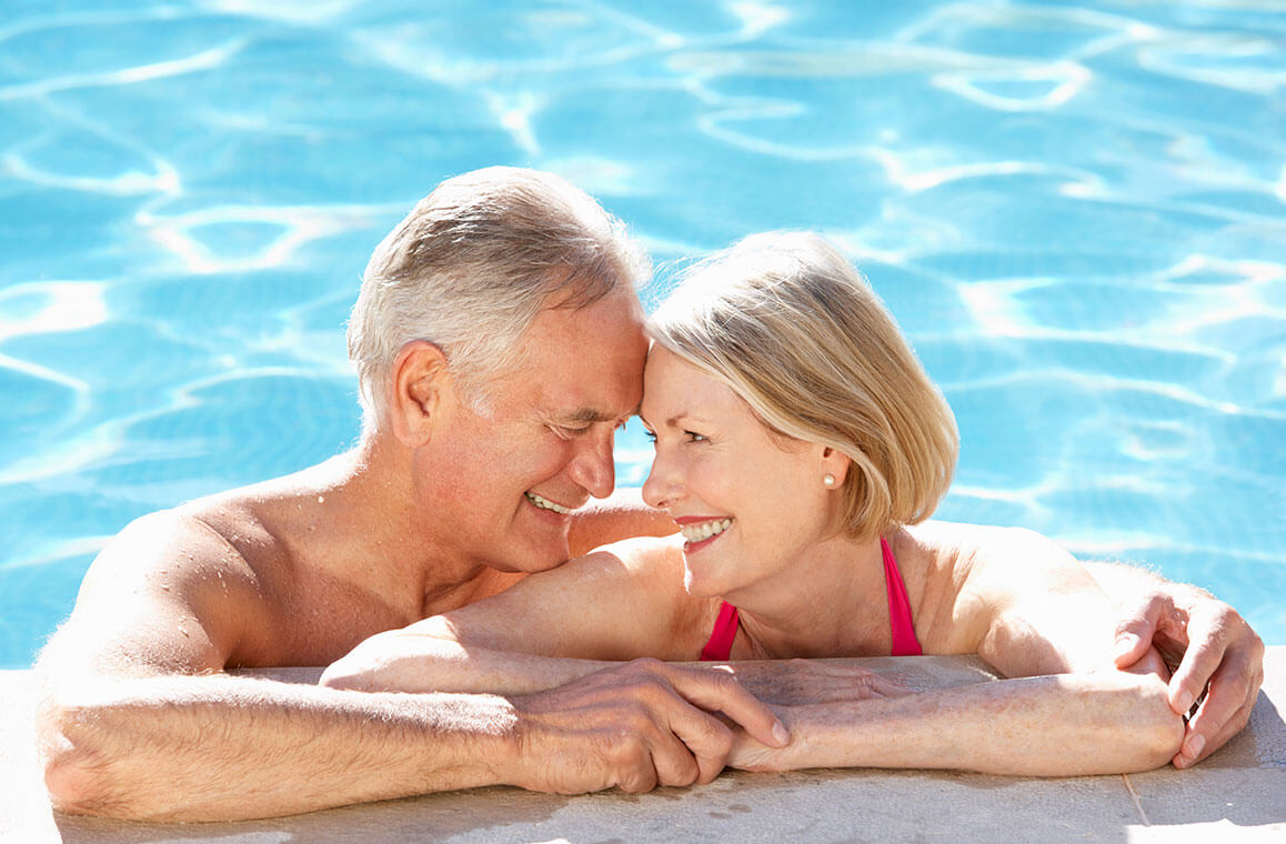 An older man and woman smiling at each other while swimming in a pool