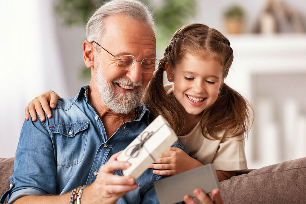 Senior man opening gift from granddaughter. Gifts to get your parents this holiday season.