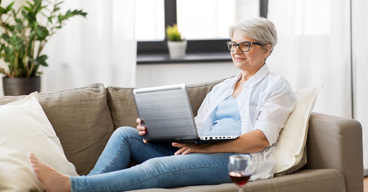 Happy senior woman laying on a couch using her laptop