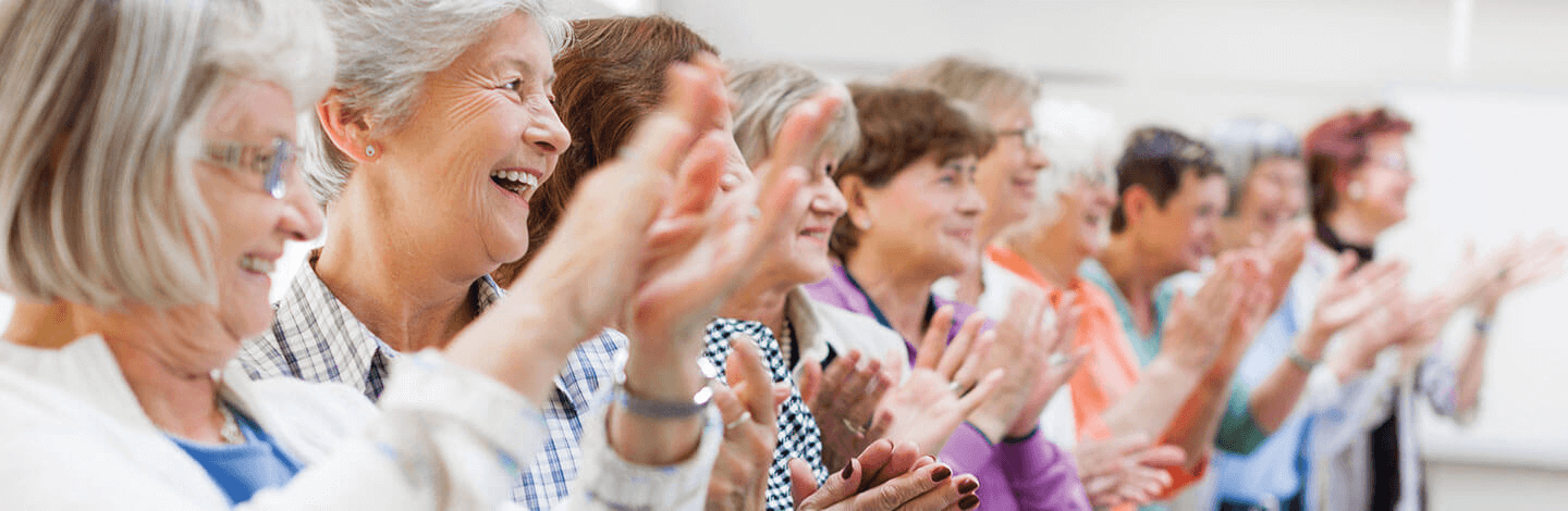 A group of female seniors stand together and clap.